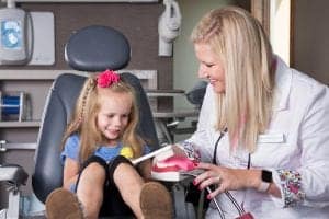 family dentist showing young girl how to brush her tongue