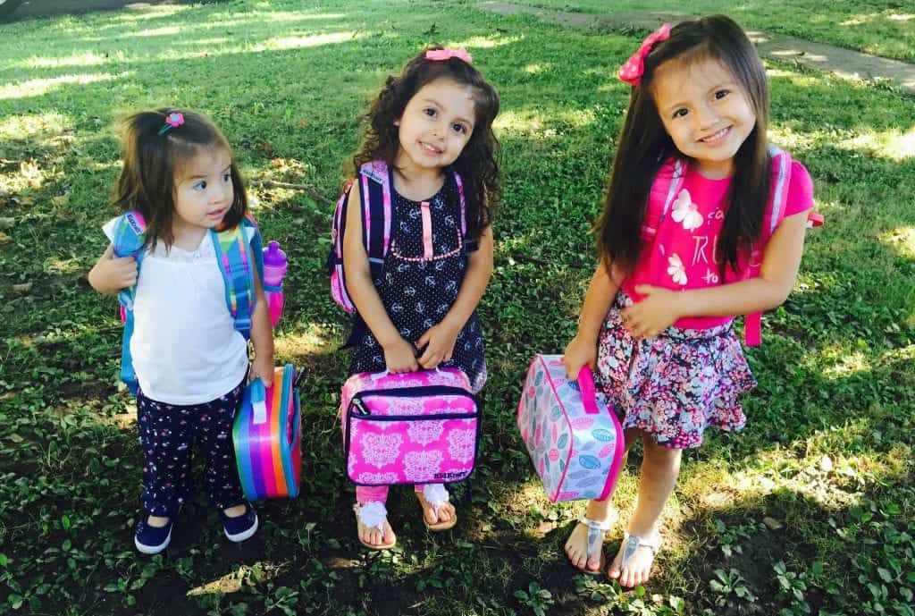 three elementary-aged girls holding lunchboxes and ready to go back to school